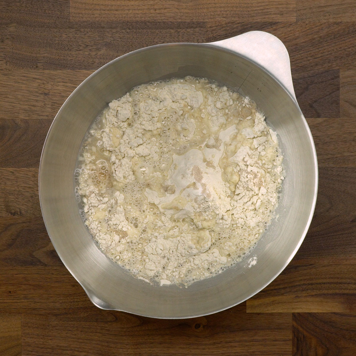 Massa de pão sendo misturada com colher em uma tigela até ficar homogênea.