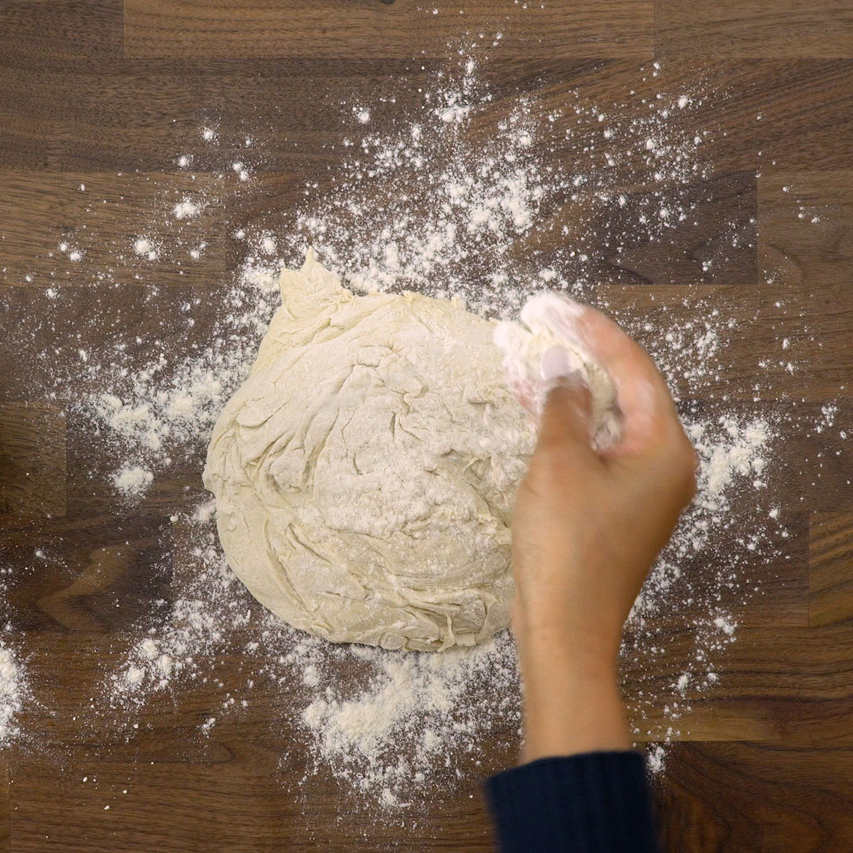 Massa de pão sendo modelada sobre superfície enfarinhada.