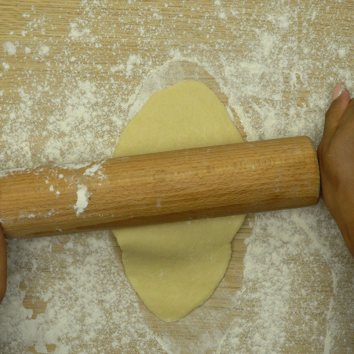 Massa de biscoito aberta com rolo sobre superfície enfarinhada.