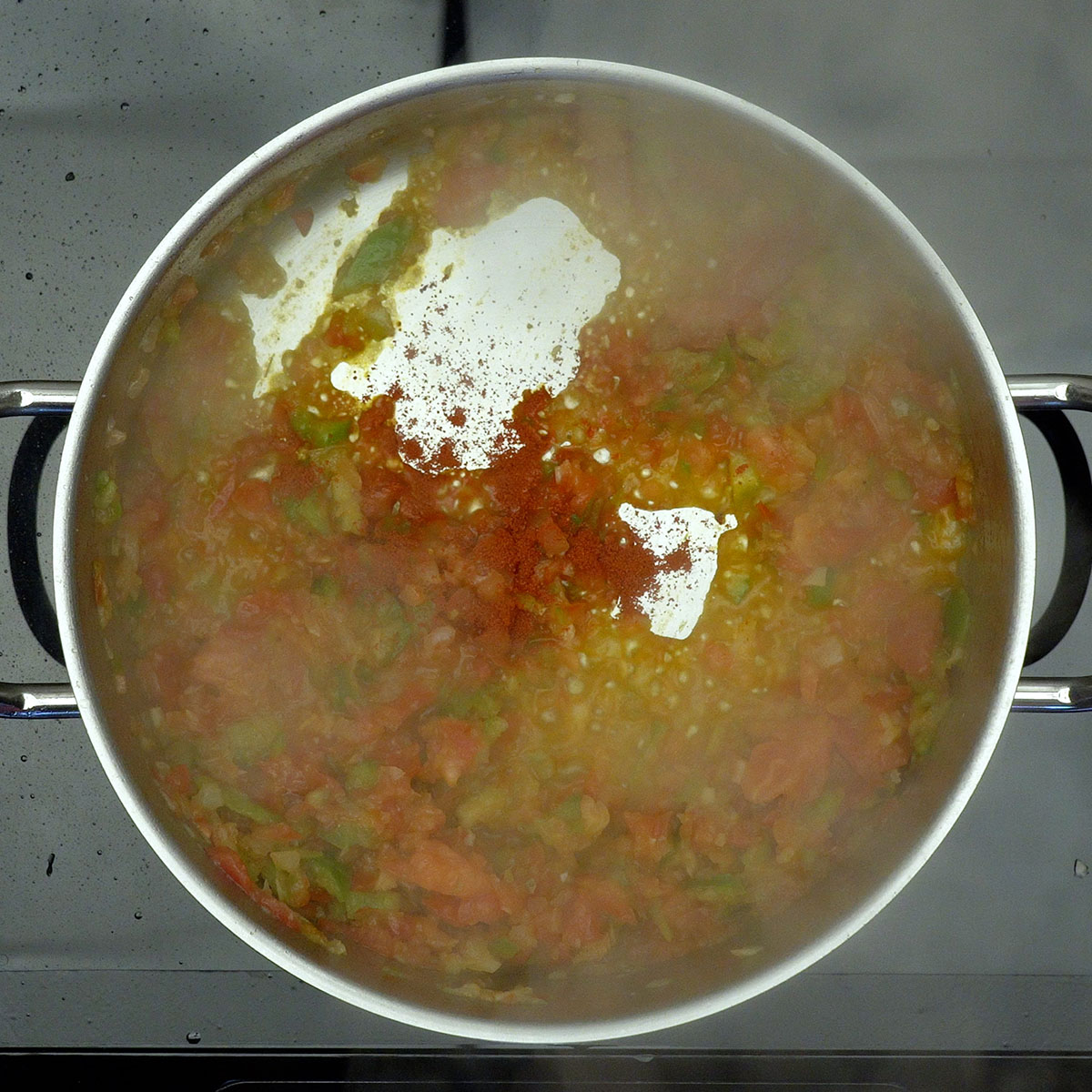 Tomate e pimentão refogando com temperos na panela.