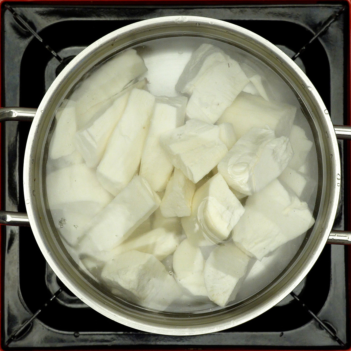 Mandioca descascada cozinhando em panela com água até amolecer.