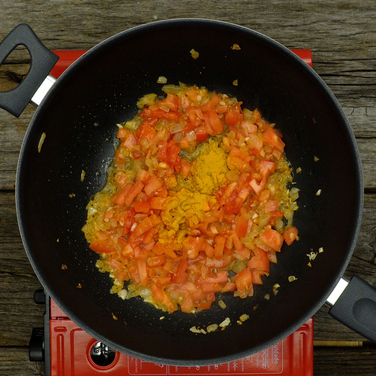 Mistura de tomate e temperos refogando na panela com cor dourada.