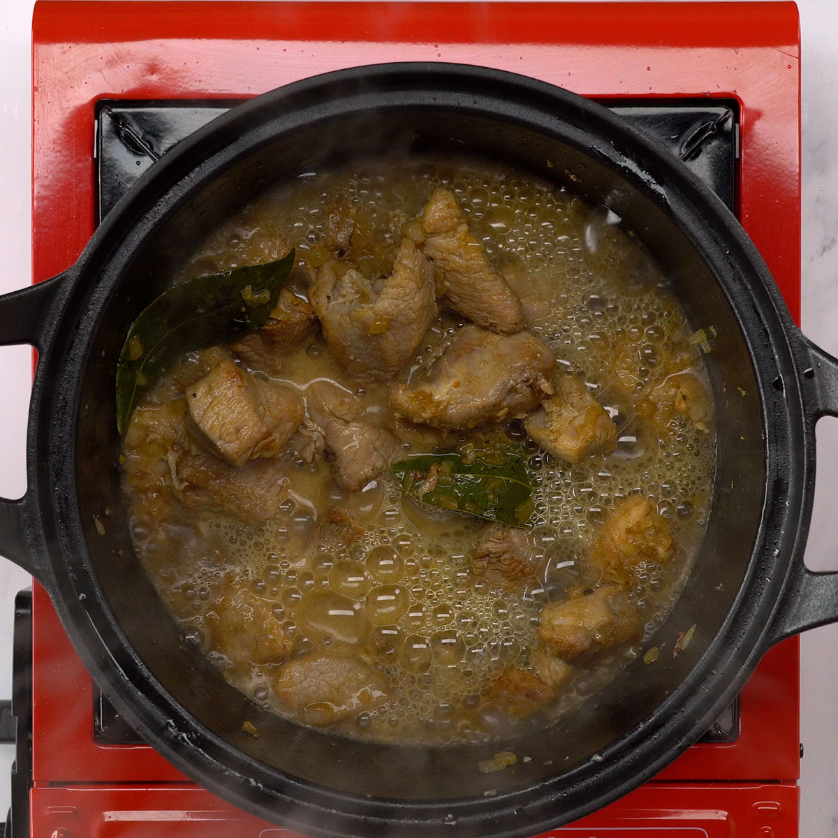 Cerveja preta sendo adicionada à carne suína na panela.