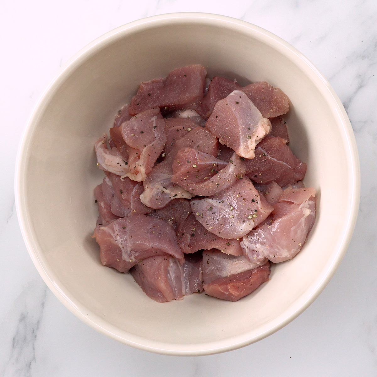 Cubos de lombo suíno temperados com sal e pimenta em uma tigela.