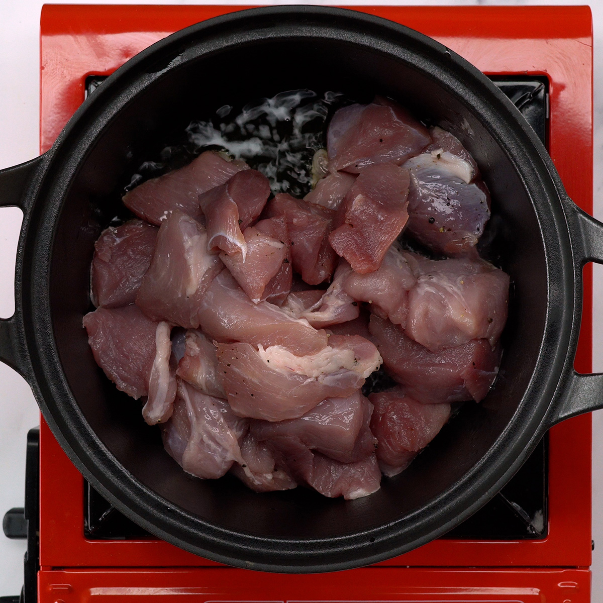 Cubos de lombo suíno dourando em uma panela com azeite quente.