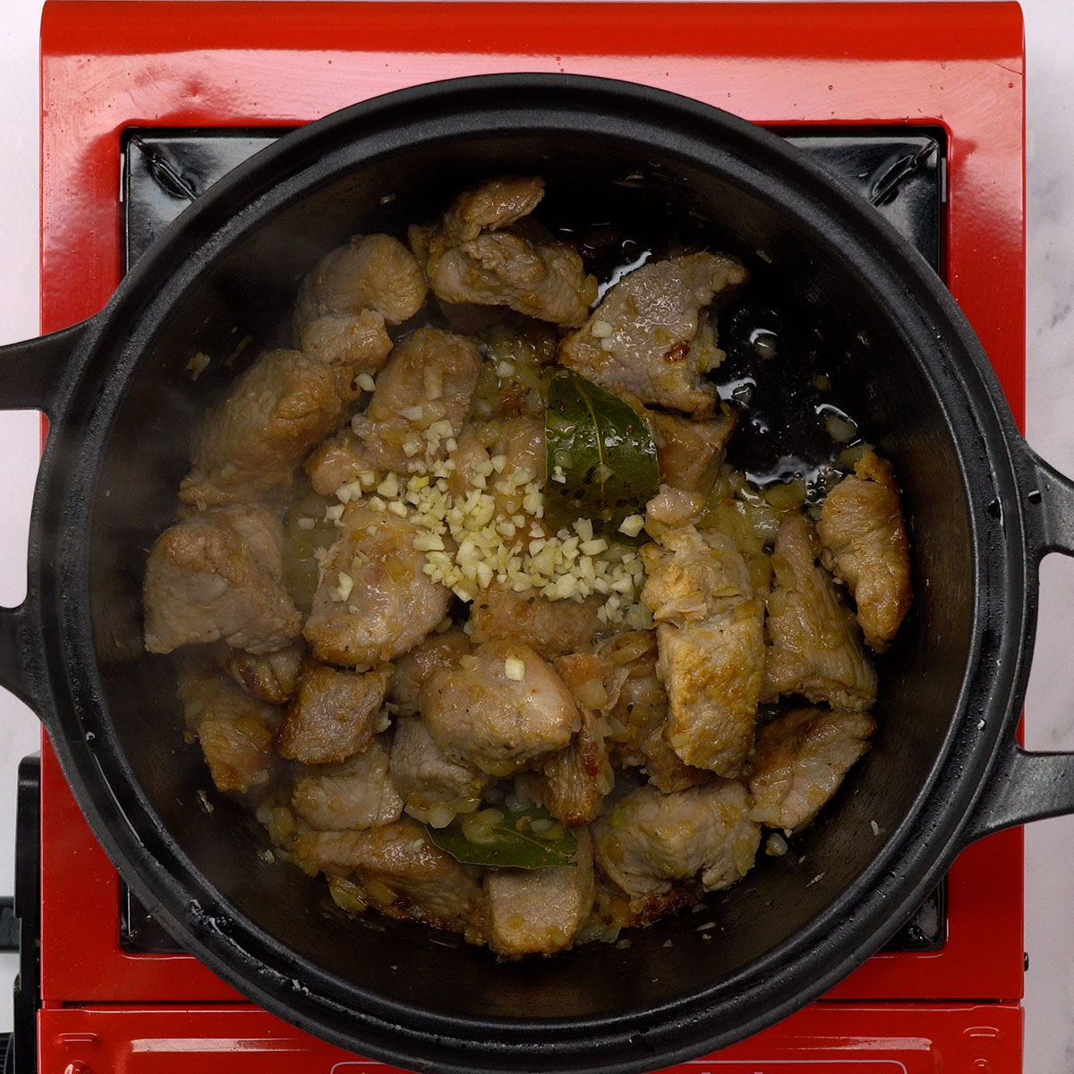 Refogado de cebola, alho e louro com carne suína na panela.