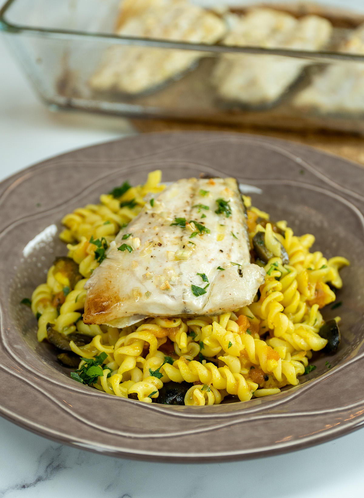 Filetes de robalo servidos com macarrão espiral ao molho.