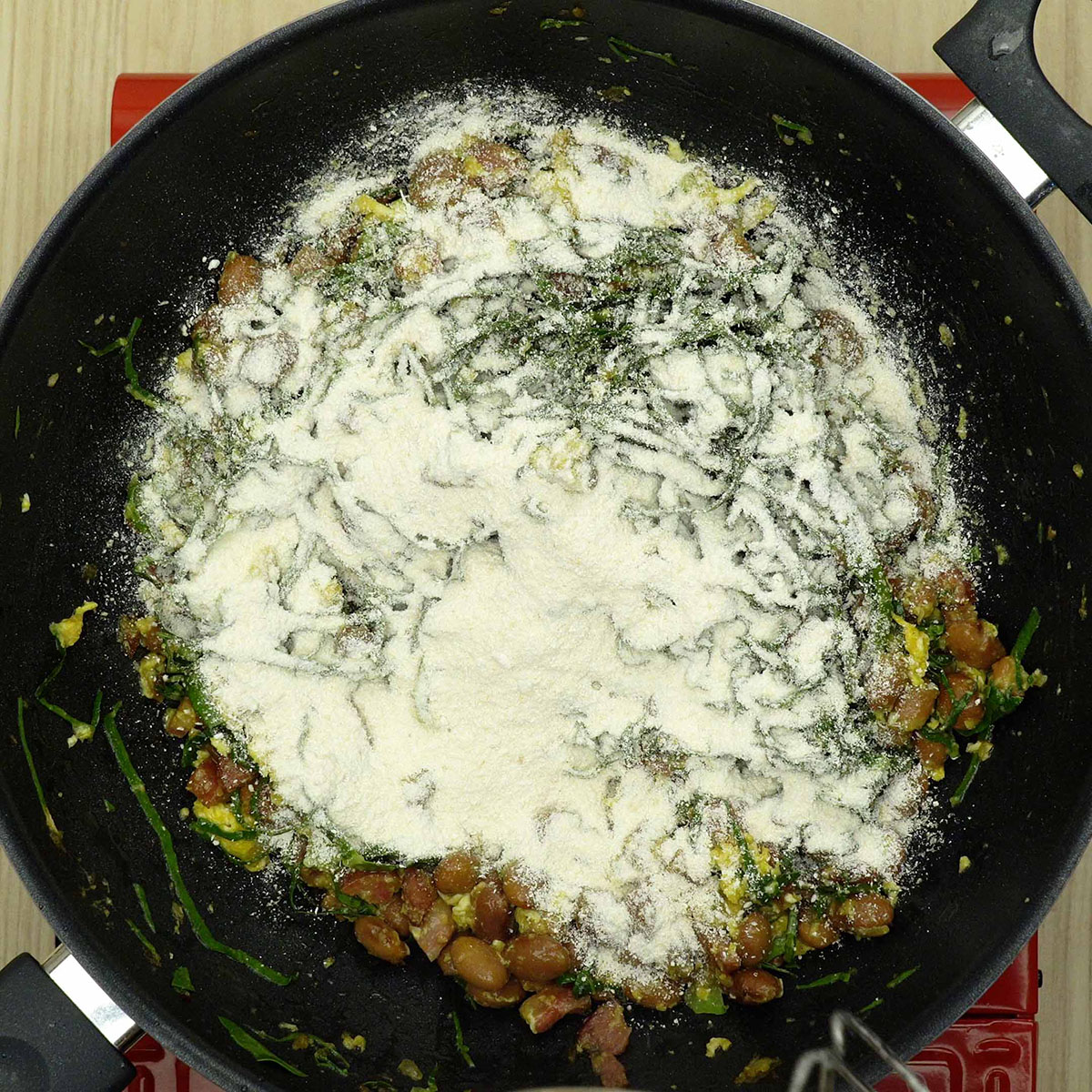 Farinha de mandioca sendo incorporada à farofa de feijão tropeiro.