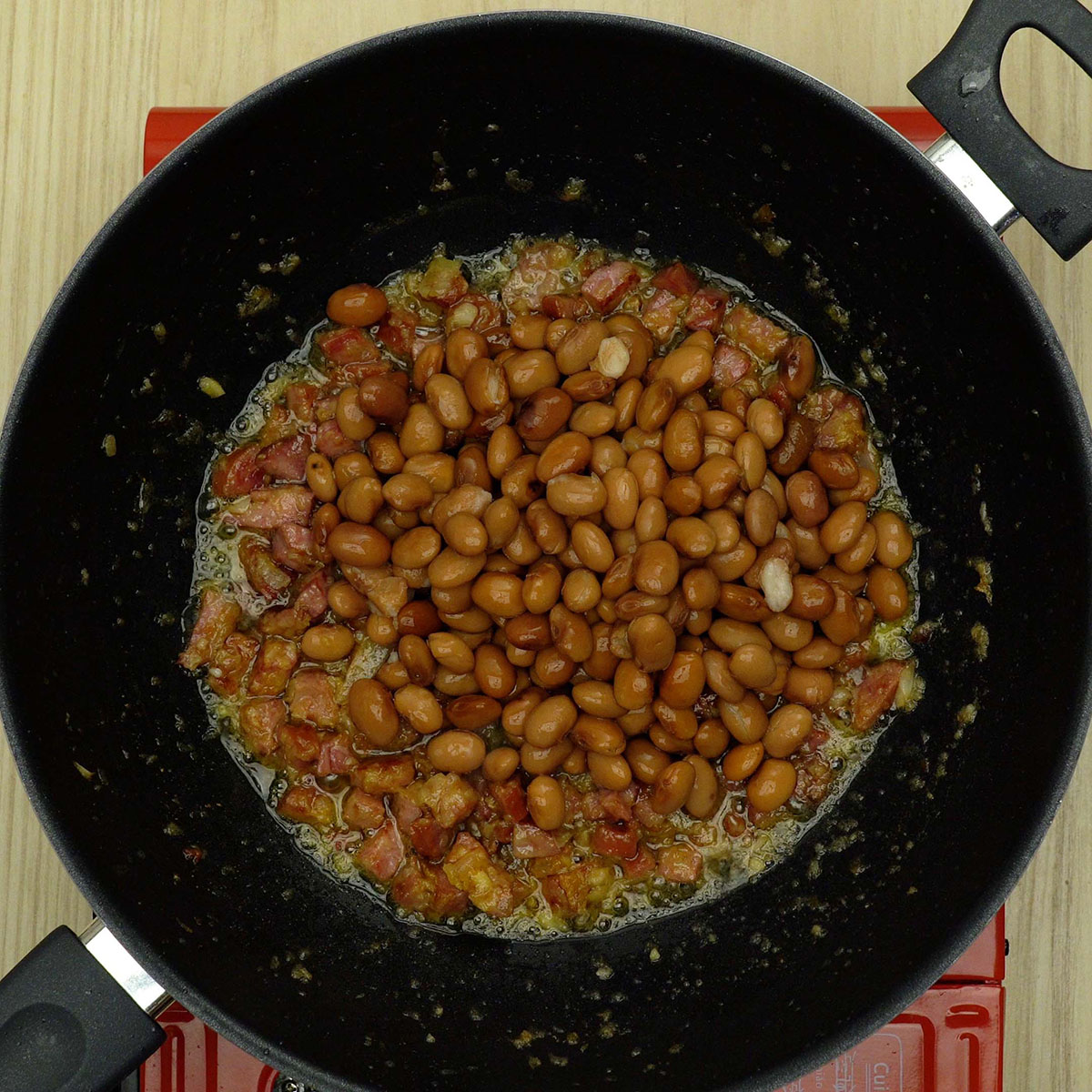 Feijão carioca sendo misturado e temperado com sal e pimenta na frigideira.