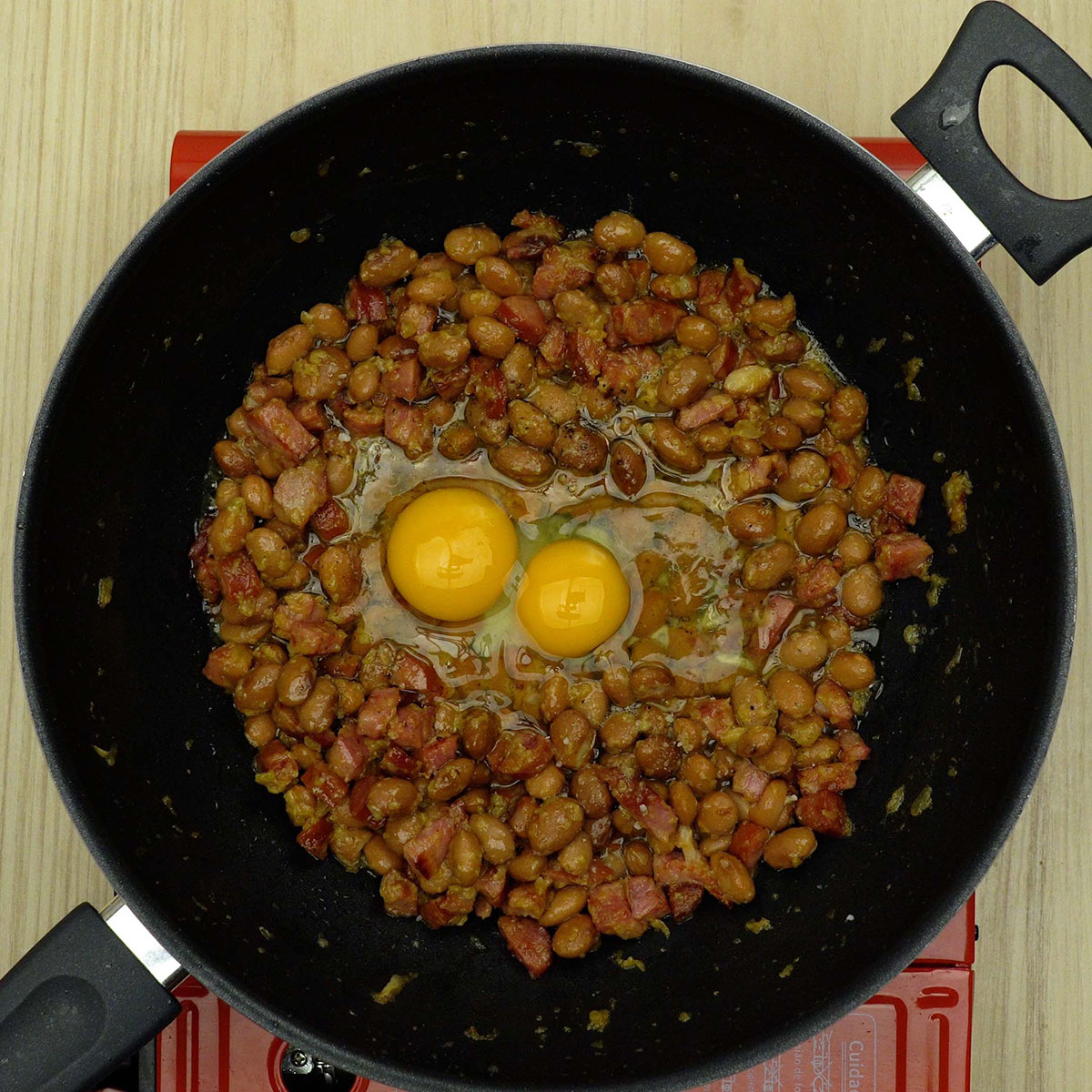 Ovos sendo incorporados à mistura de feijão tropeiro na frigideira.