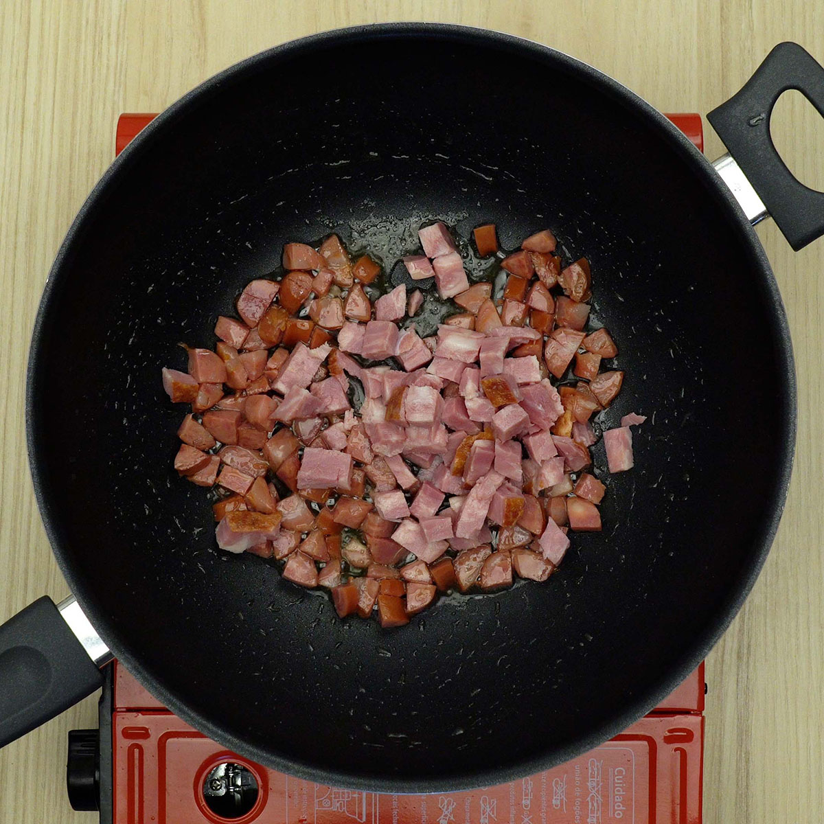 Linguiça e bacon dourando em frigideira com azeite até ficarem crocantes.