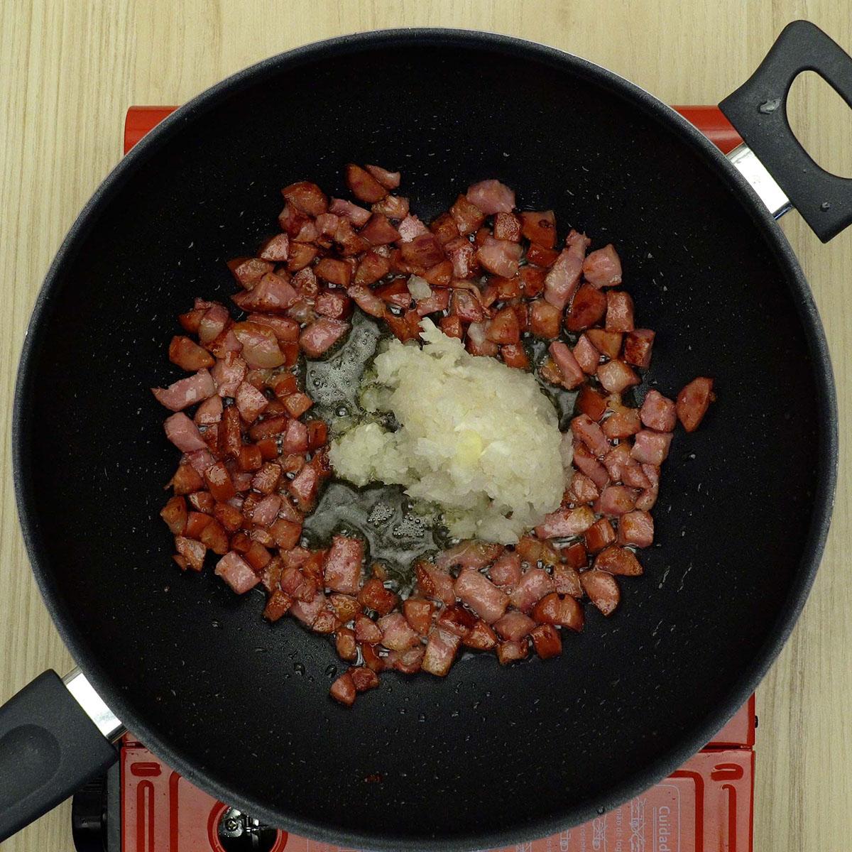 Cebola picada sendo refogada junto com bacon e linguiça na frigideira.
