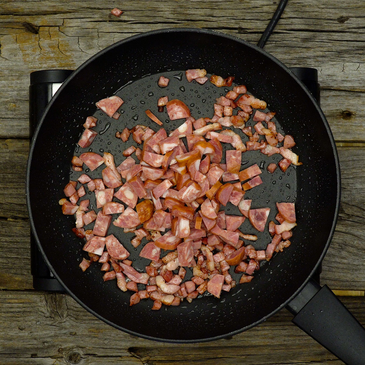 Linguiça calabresa sendo refogada com bacon dourado na frigideira.