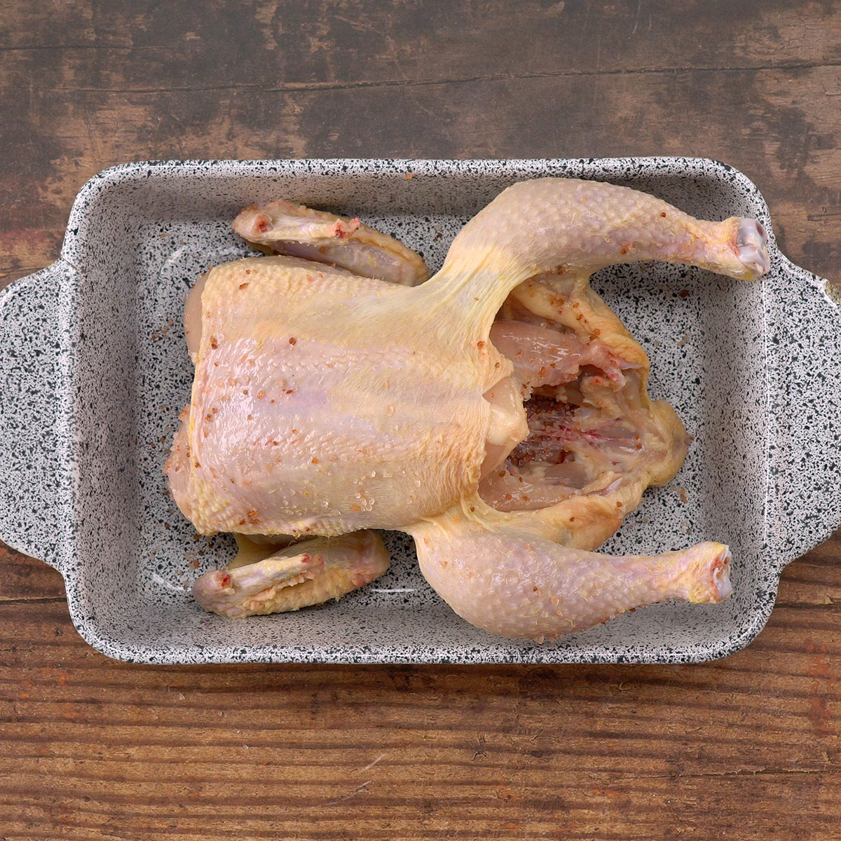 Frango inteiro sendo temperado com sal e pimenta em refratário.