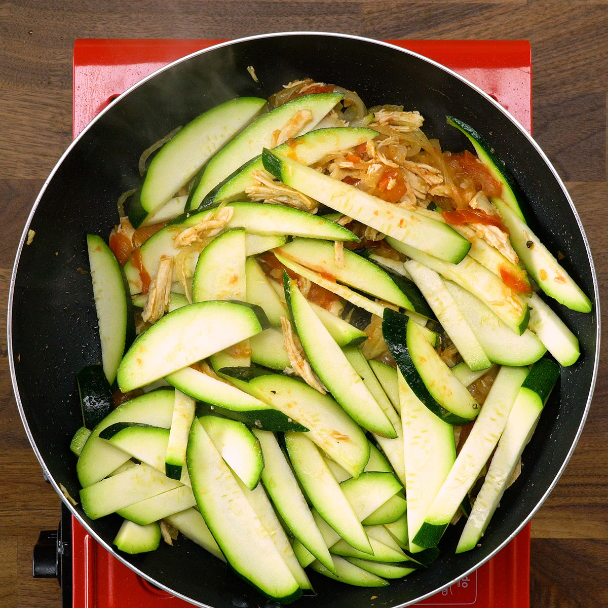 Abobrinha fatiada sendo adicionada ao frango na frigideira.