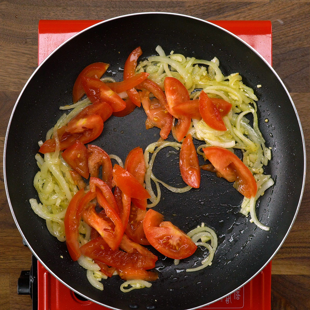 Alho e tomate sendo refogados juntos na frigideira.