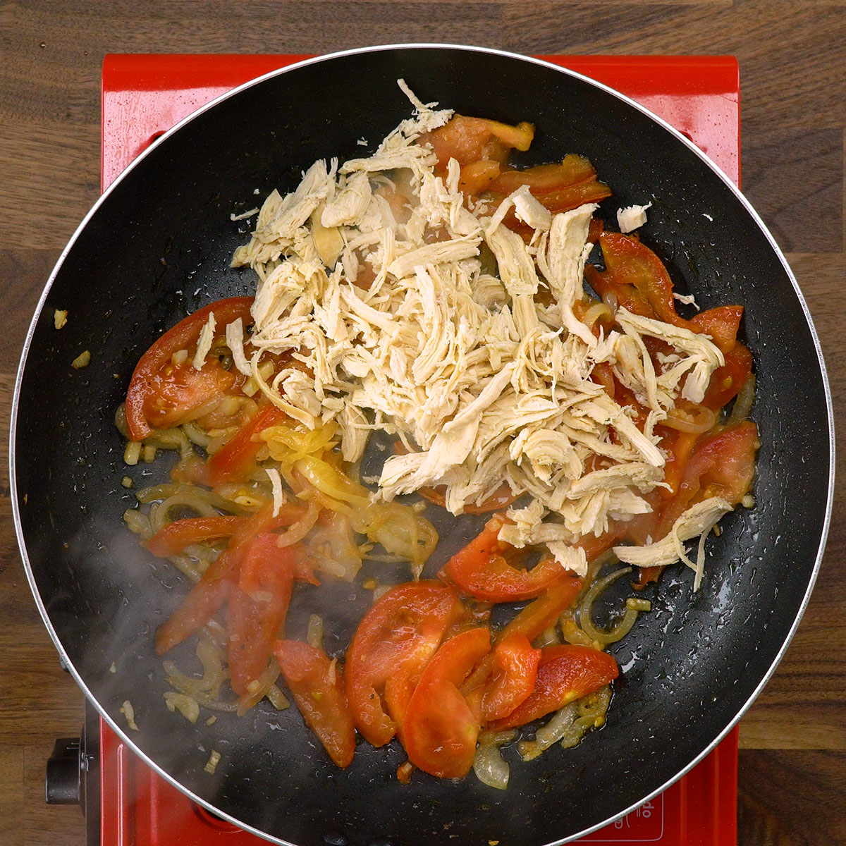 Frango desfiado misturado ao refogado na frigideira.