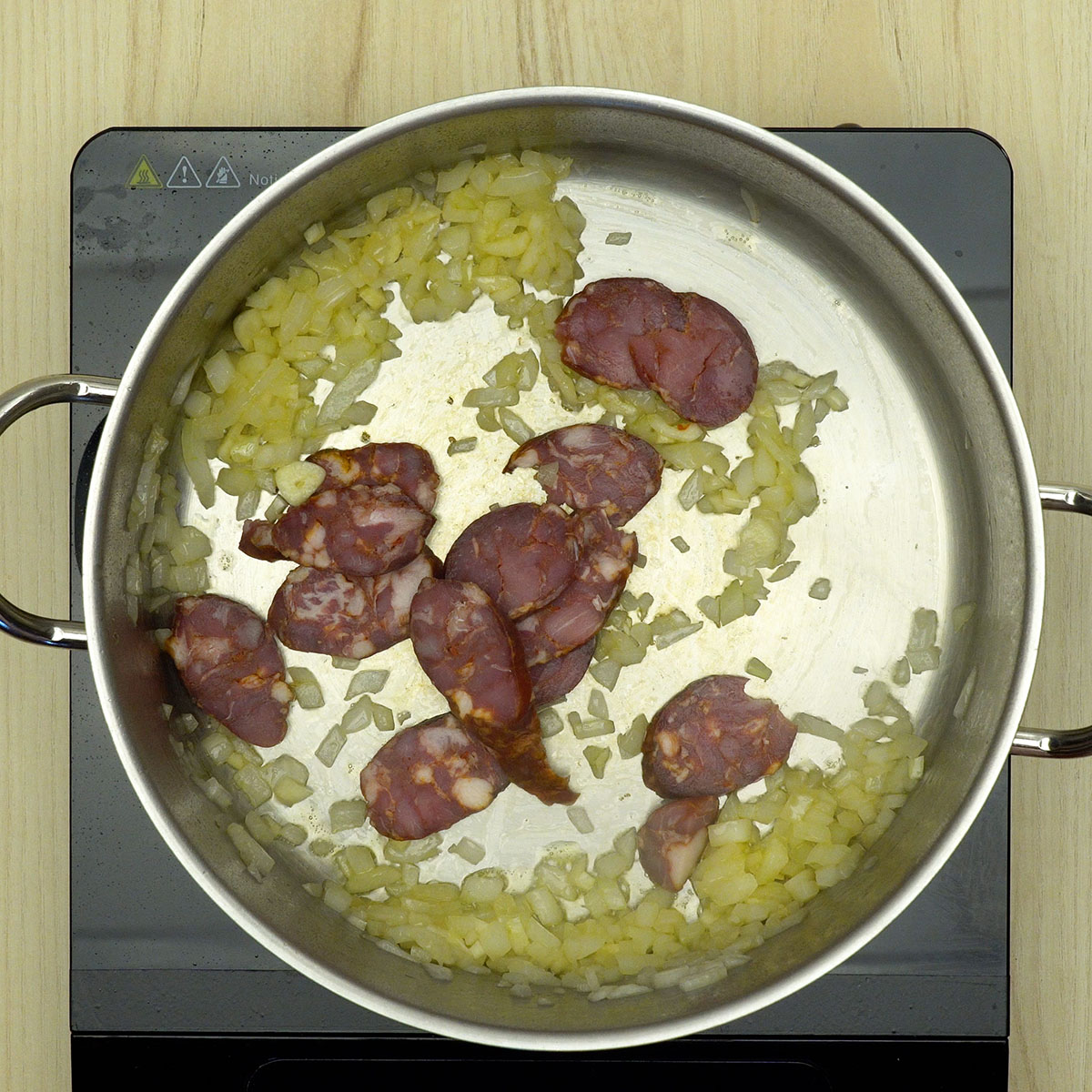 Linguiça com cebola e alho sendo refogada até dourar.