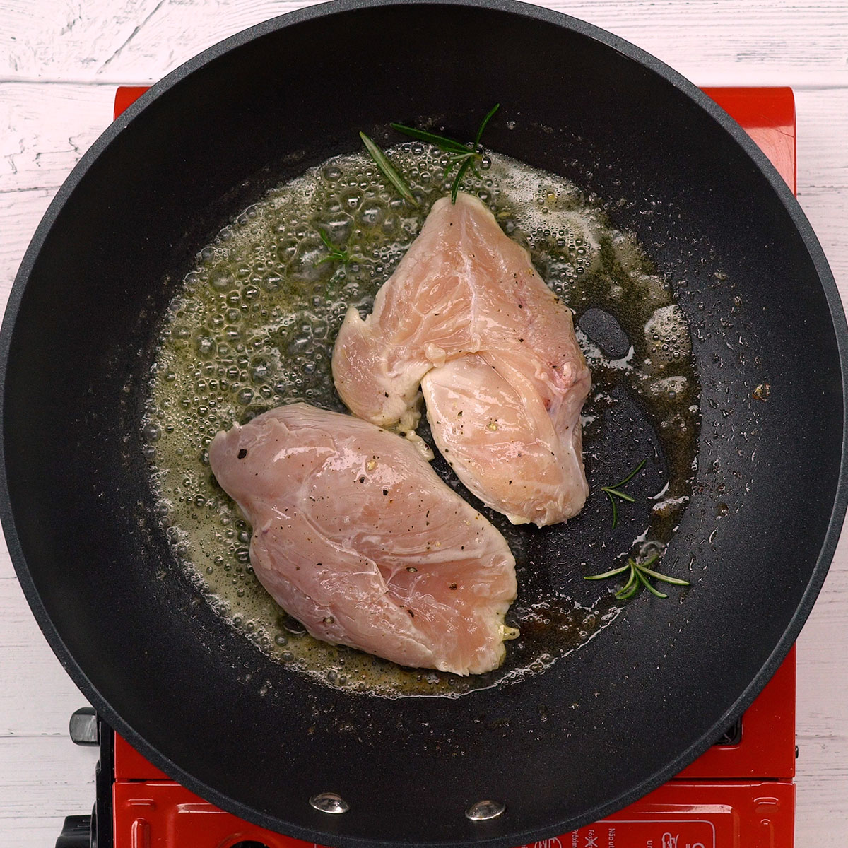 Peito de frango dourando com alecrim em frigideira quente.
