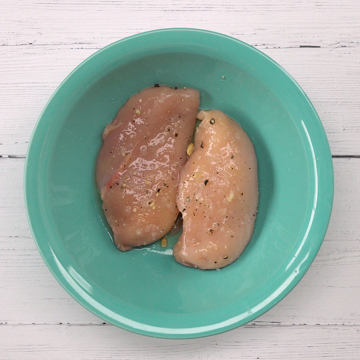 Peito de frango sendo temperado com limão, sal e pimenta em tigela.