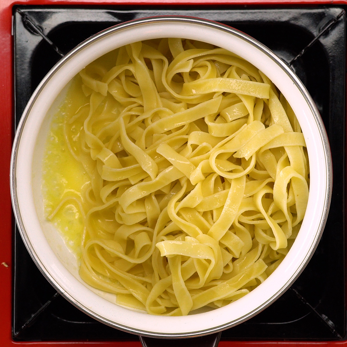 Tagliatelle sendo envolvido com manteiga na panela.