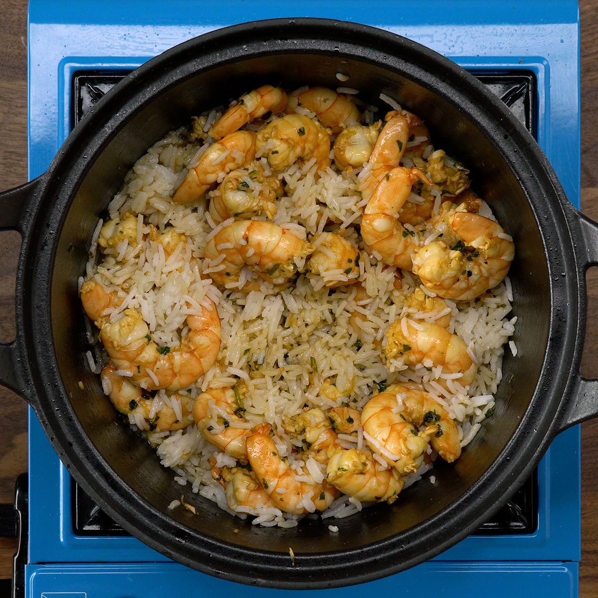 Arroz cozido sendo misturado aos camarões dourados na panela.