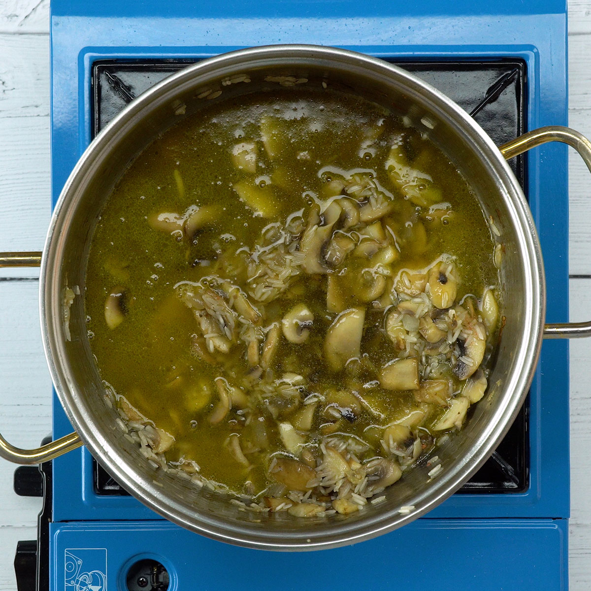 Caldo de legumes sendo adicionado ao arroz de cogumelos.