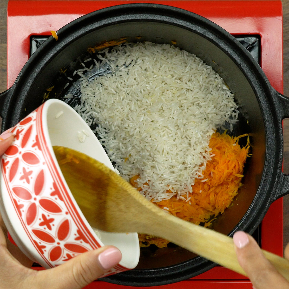 Arroz branco sendo misturado ao refogado de alho e cenoura na panela.