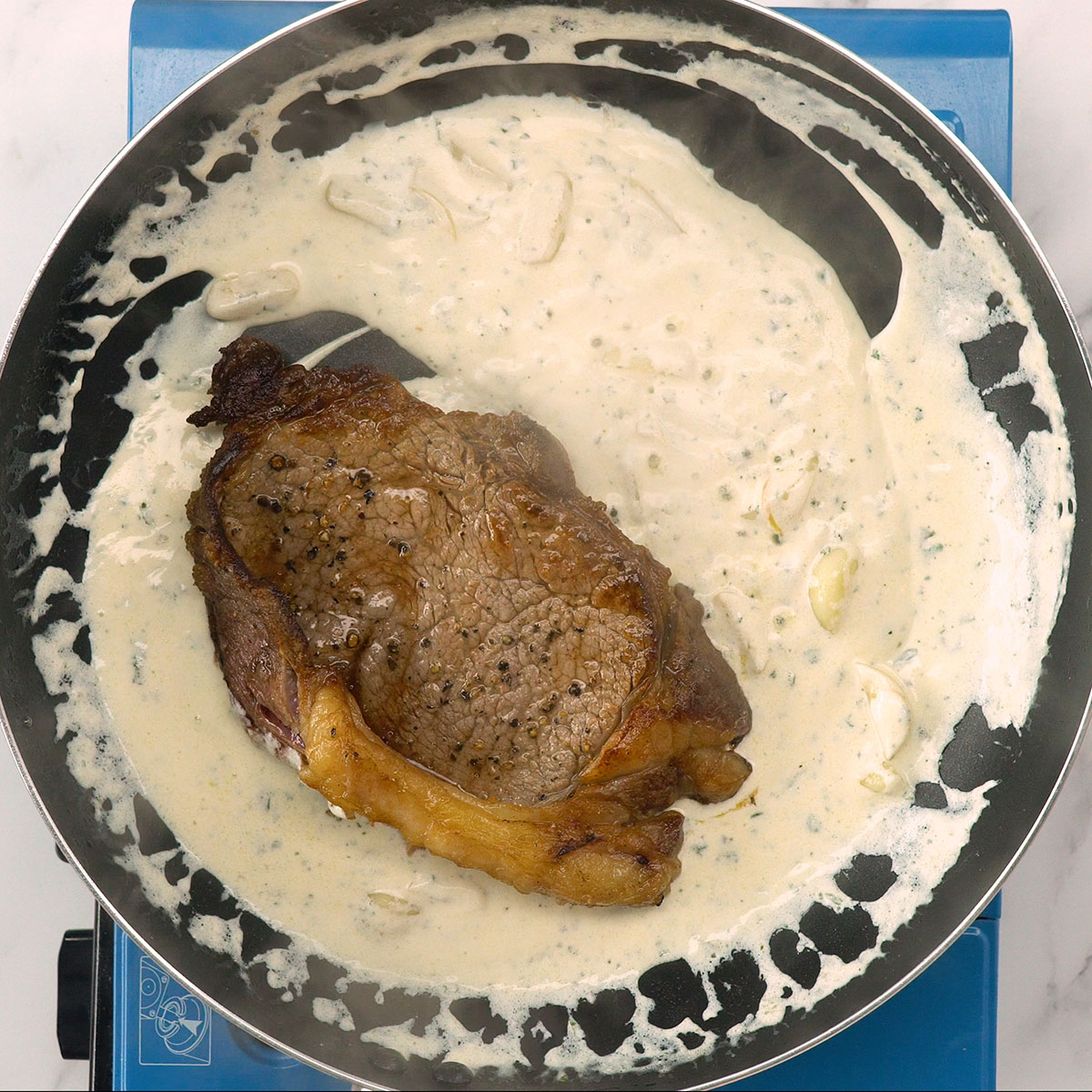 Bife coberto com molho cremoso de alho na frigideira.