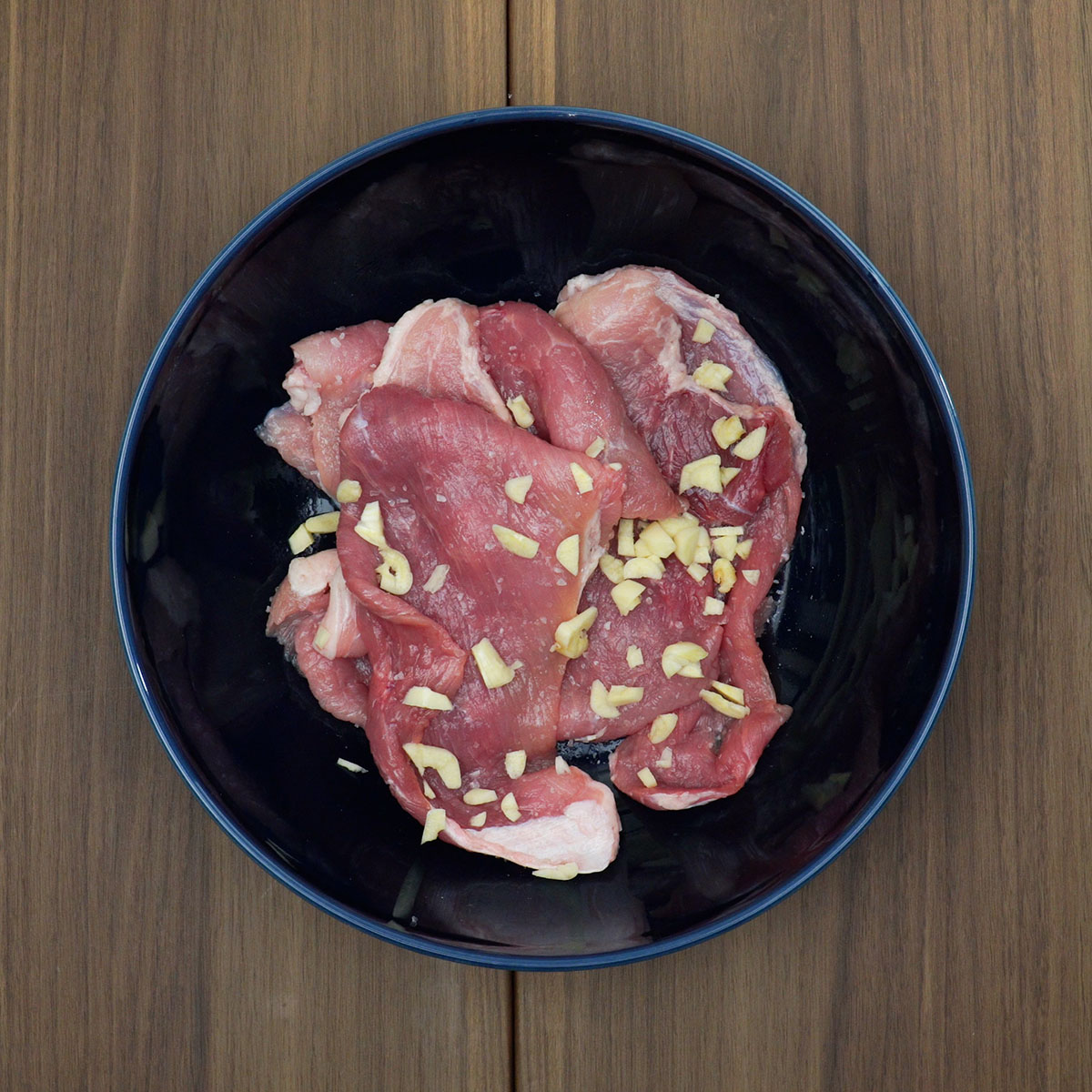 Bifes de porco sendo temperados com sal e alho picado.
