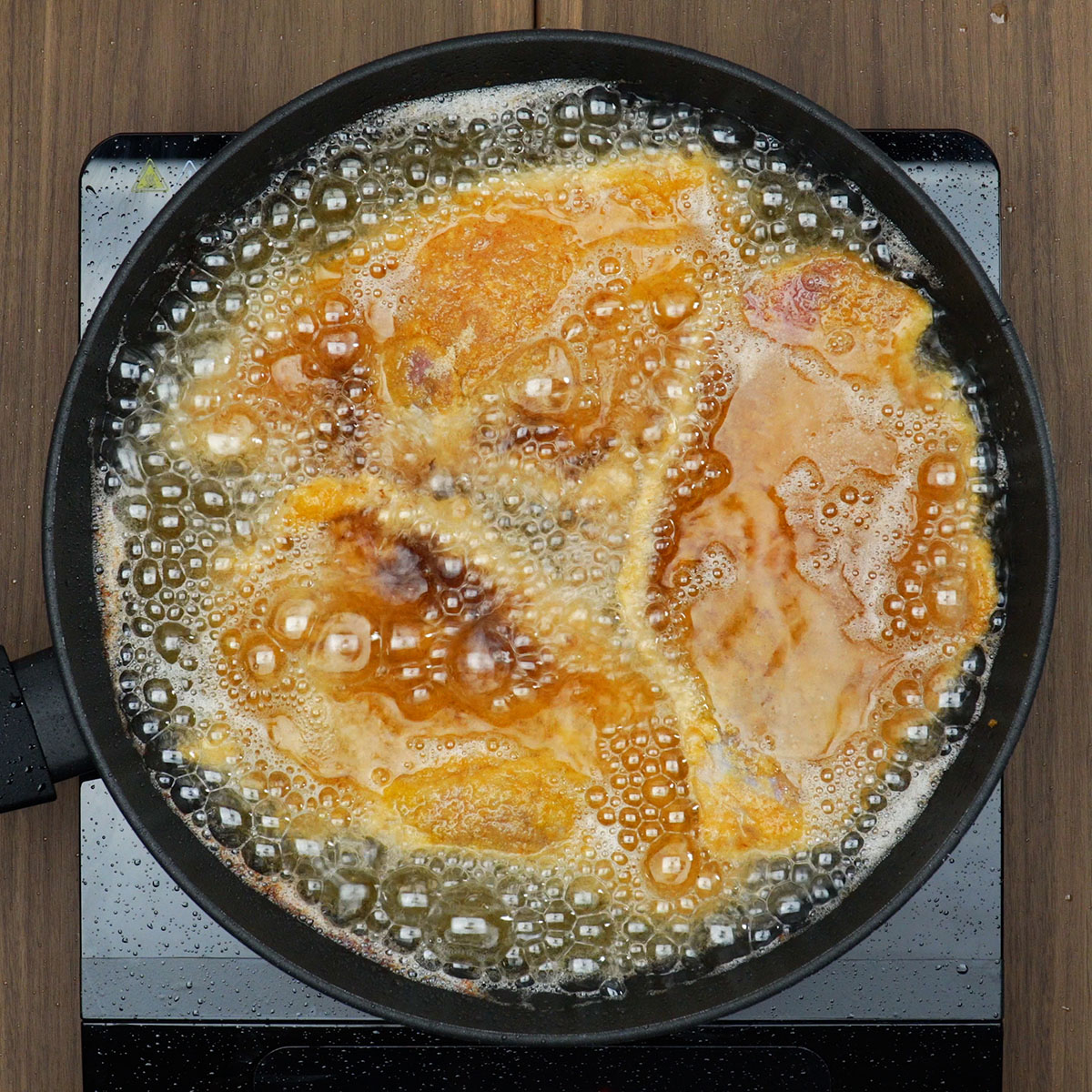 Bifes de porco fritando em óleo quente até dourar.