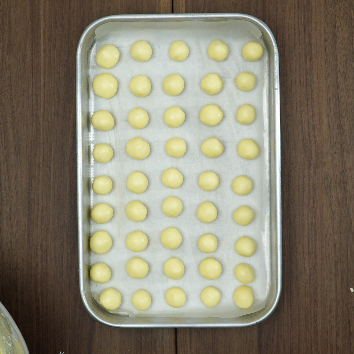 Bolinhas de massa sendo modeladas e distribuída em uma assadeira untada para assar os biscoitos caseiros.