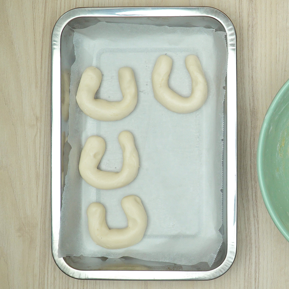 Massa de biscoito de polvilho modelada em formato de ferradura sobre assadeira.