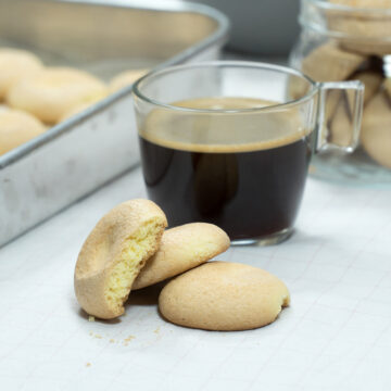 Biscoitos de fubá prontos acompanhado de uma xícara de café.