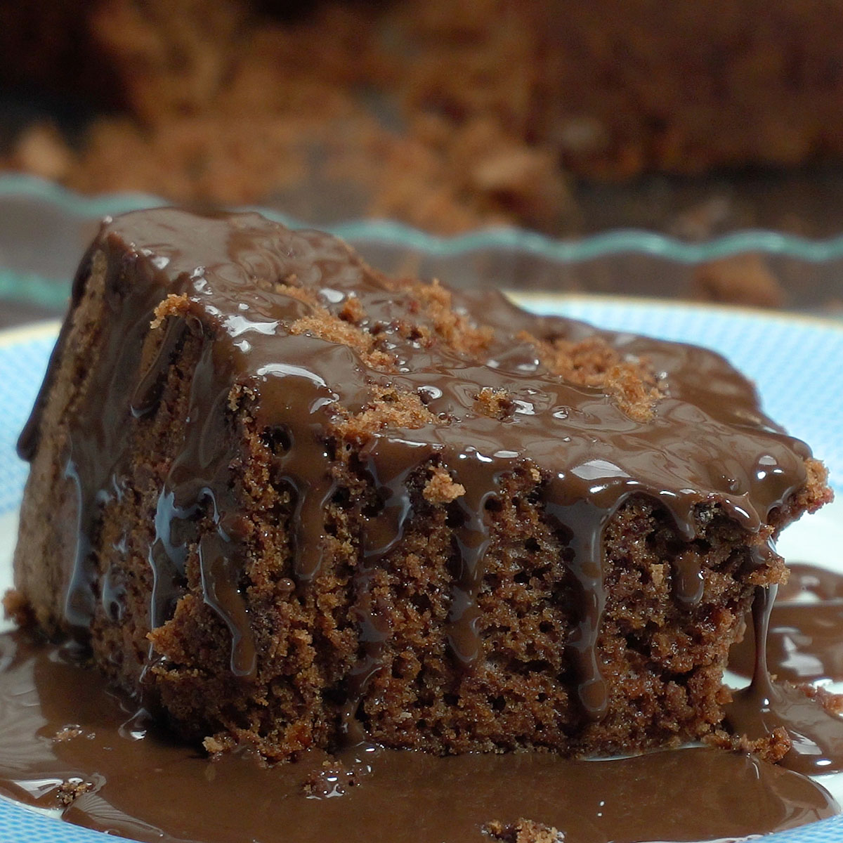 Fatia de bolo de chocolate servida no prato com calda de chocolate por cima.
