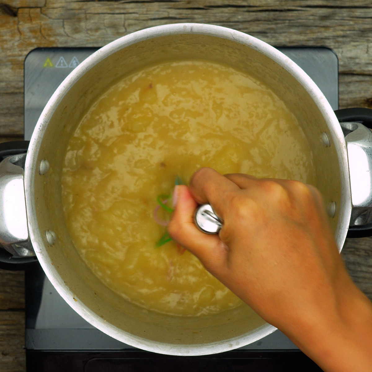 Mandioca sendo amassada dentro da panela formando caldo espesso.