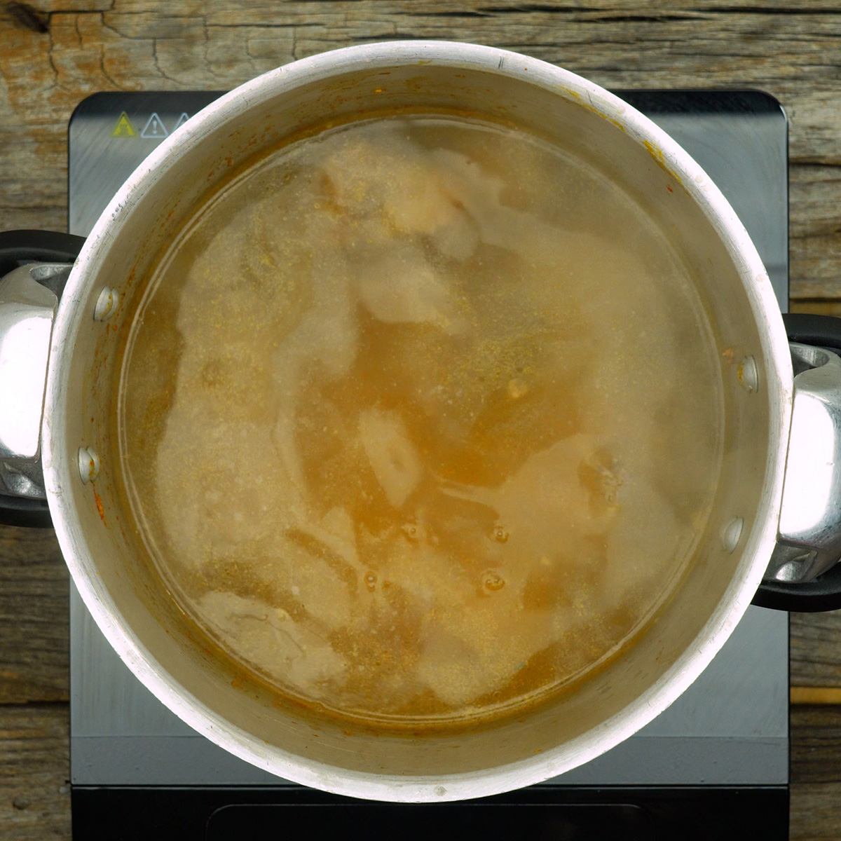 Costela bovina cozinhando com colorau e caldo avermelhado na panela de pressão.