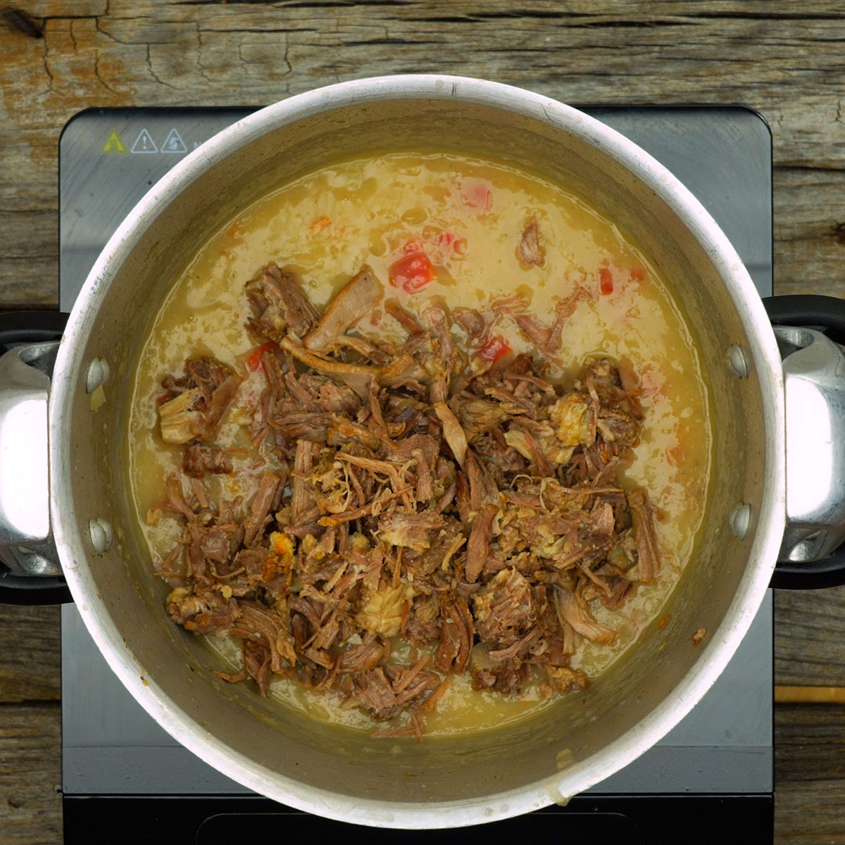 Caldo de mandioca sendo misturado com tomates e costela desfiada.