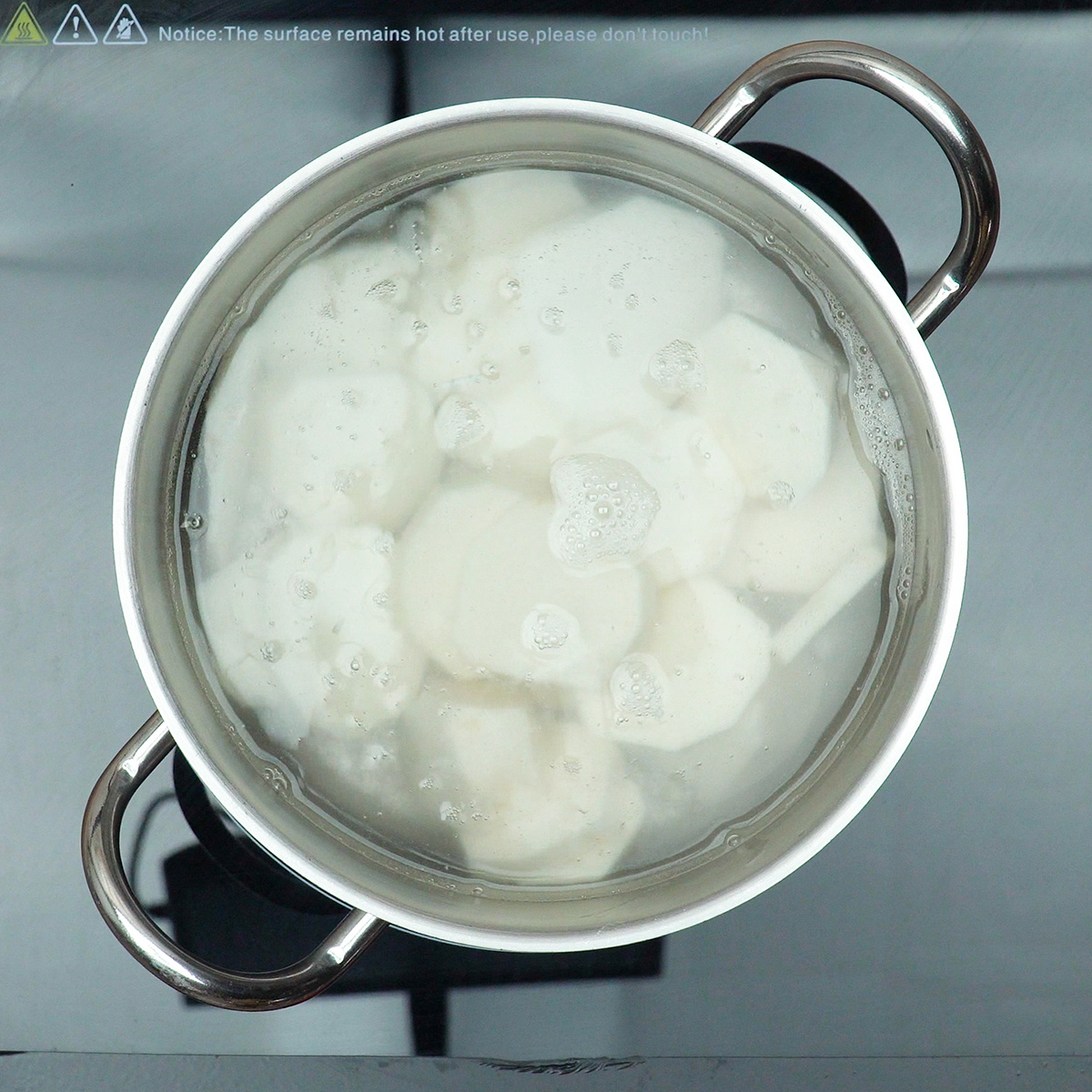 Pedaços de inhame cozinhando em panela com água até ficarem macios.