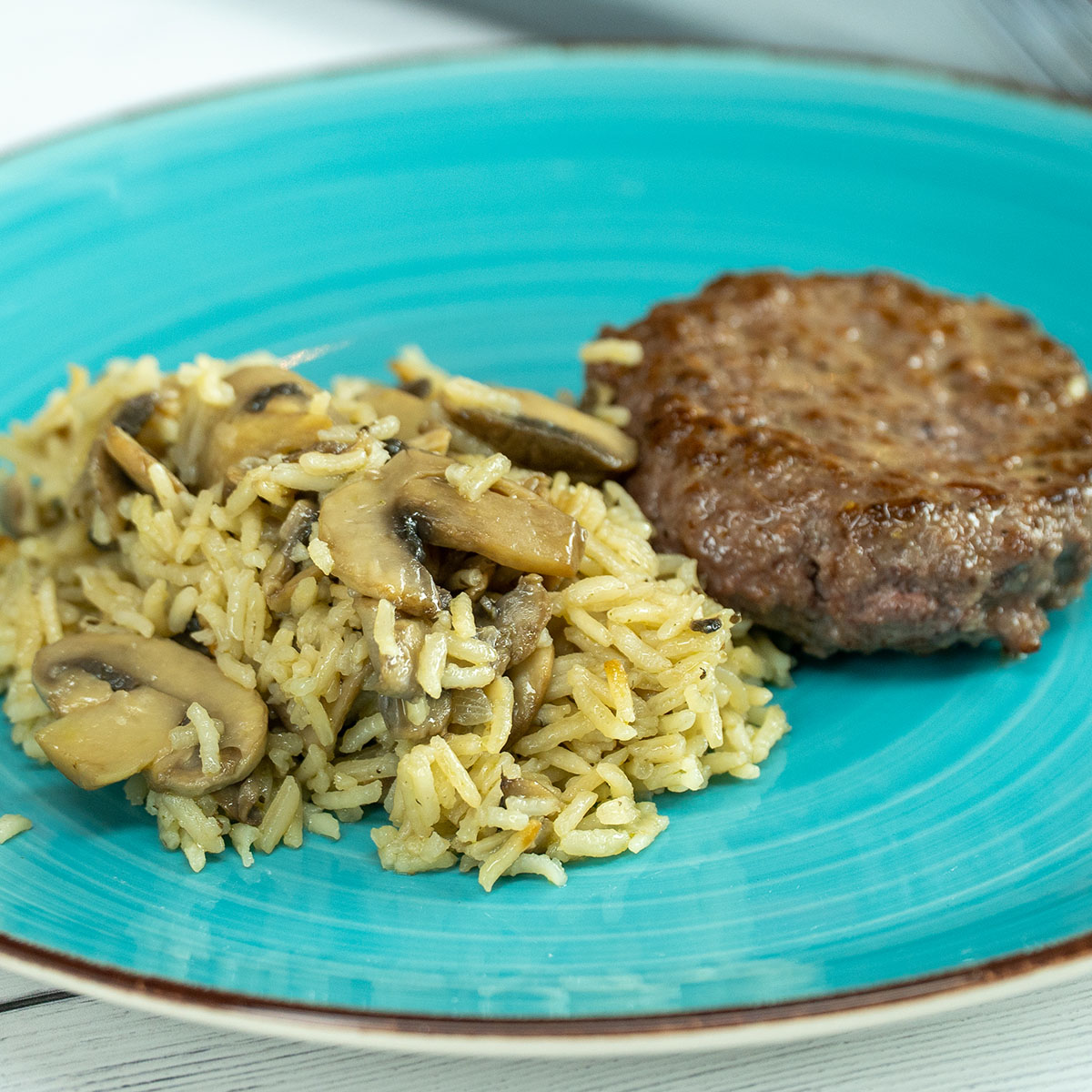 Empratamento arroz de cogumelos com hambúrguer servido.
