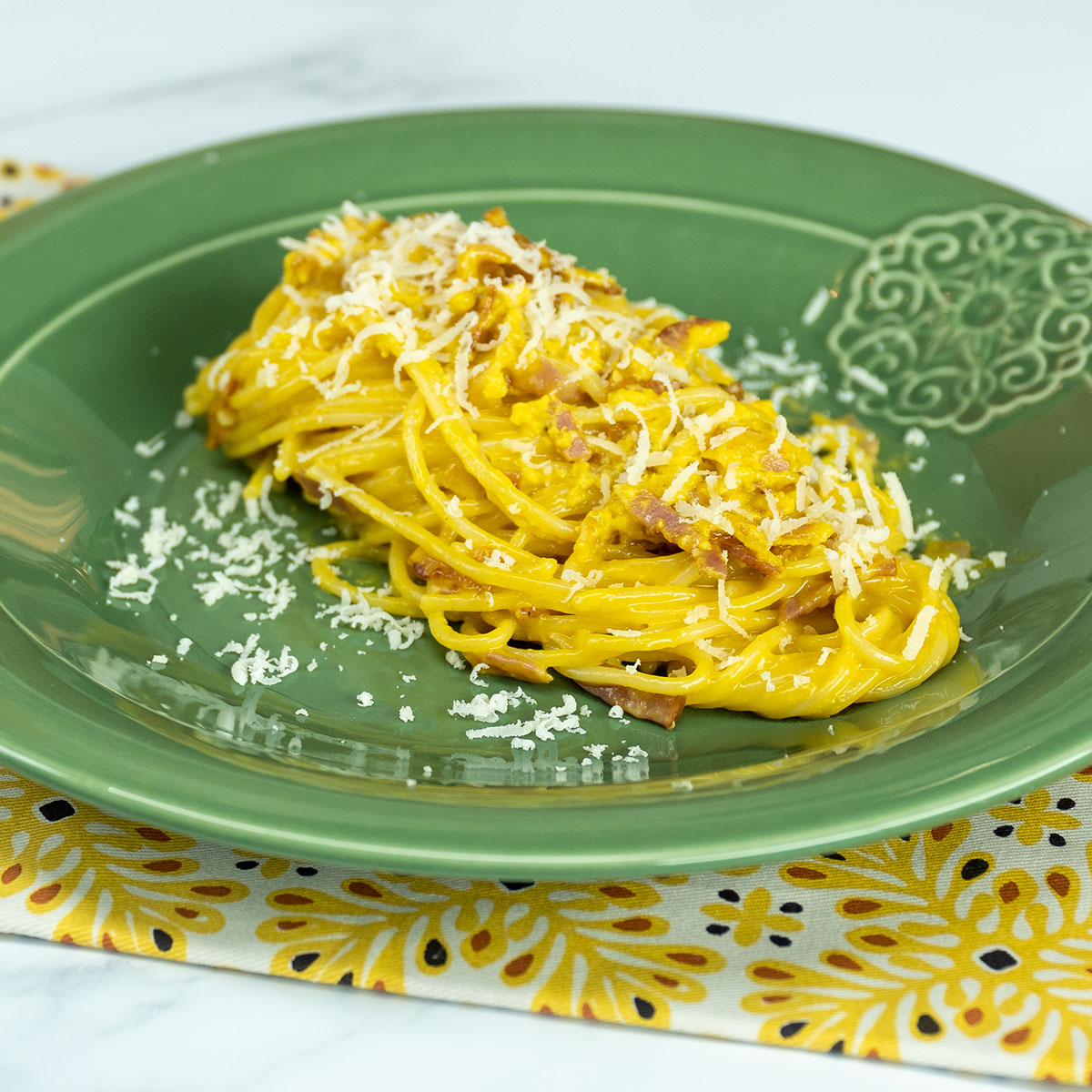Empratamento espaguete à carbonara finalizado com queijo parmesão ralado.