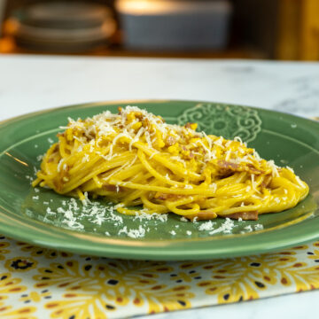 Empratamento espaguete à carbonara finalizado com queijo parmesão ralado.