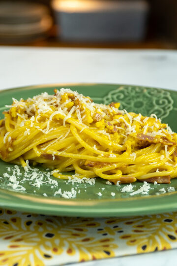 Empratamento espaguete à carbonara finalizado com queijo parmesão ralado.