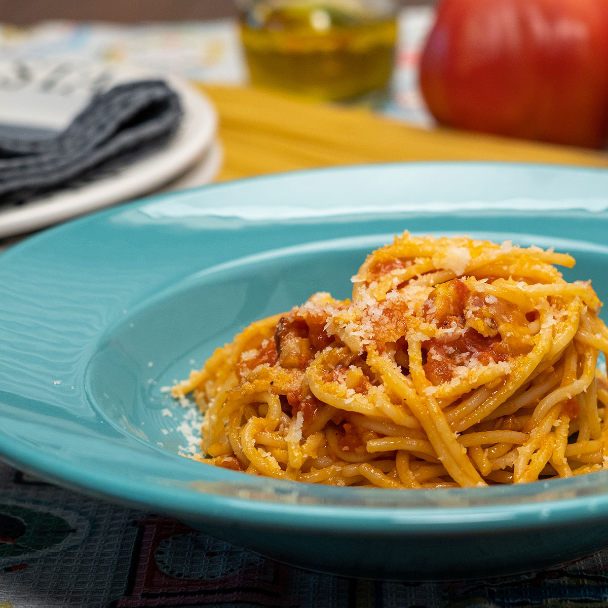 Empratamento espaguete amatriciana com queijo parmesão ralado por cima.