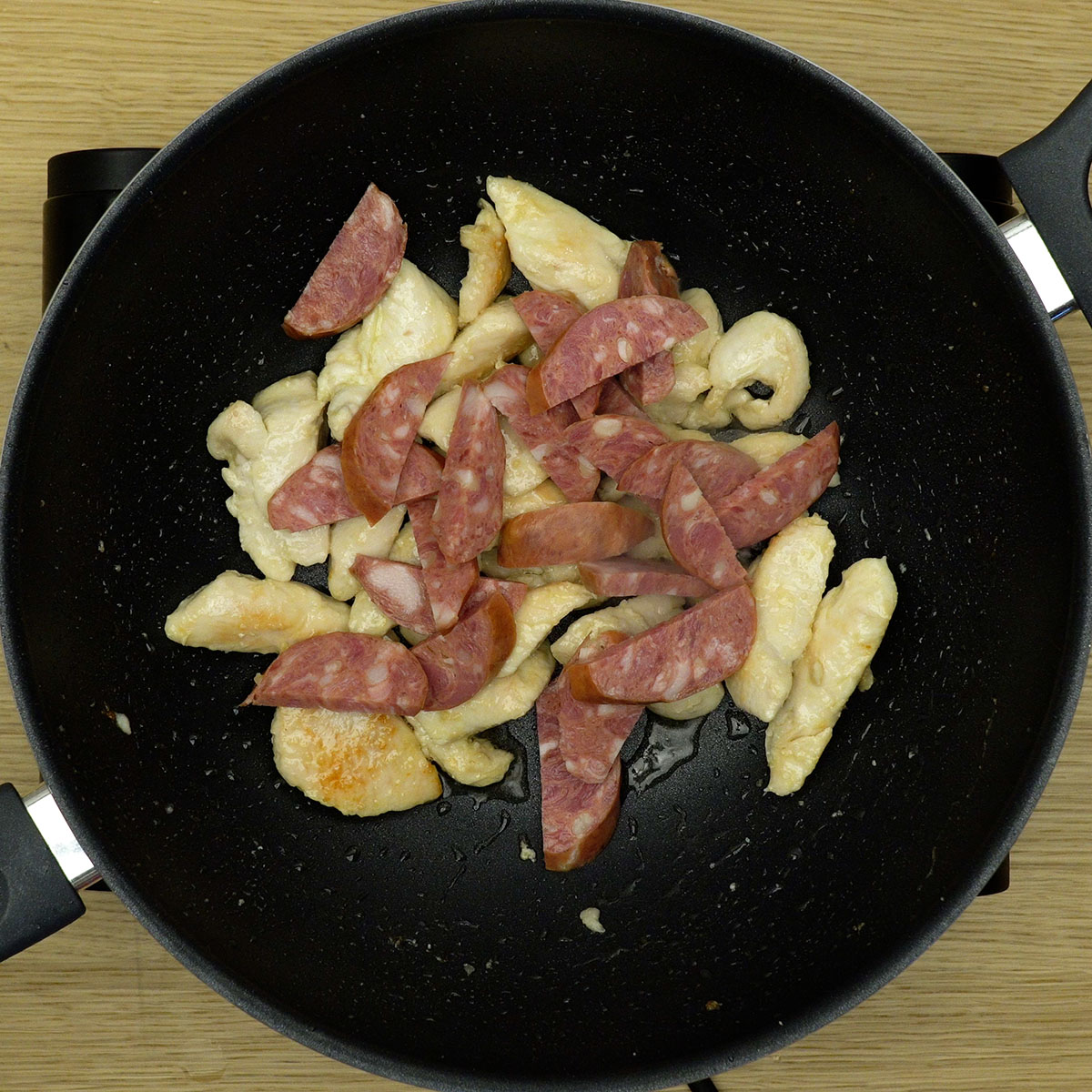 Linguiça calabresa dourando junto com frango na frigideira.