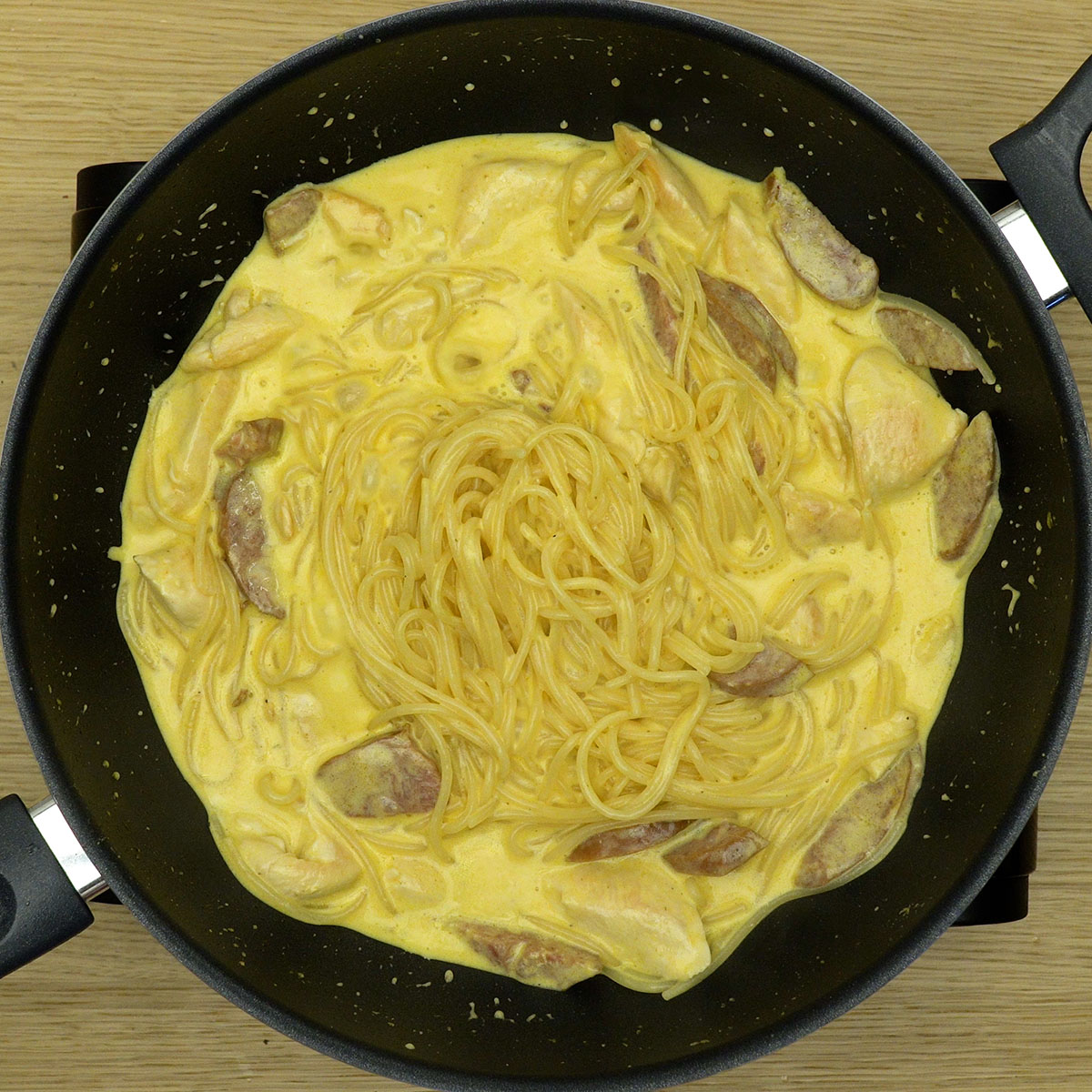 Espaguete cozinhando no molho cremoso com frango e calabresa.