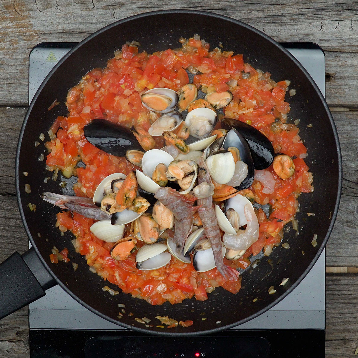 Mistura de mariscos sendo adicionada ao refogado de tomate.