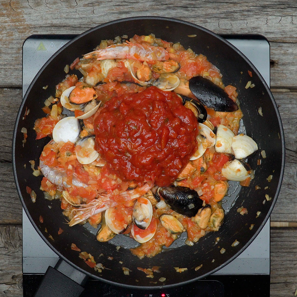 Molho de tomate sendo incorporado ao preparado de mariscos.