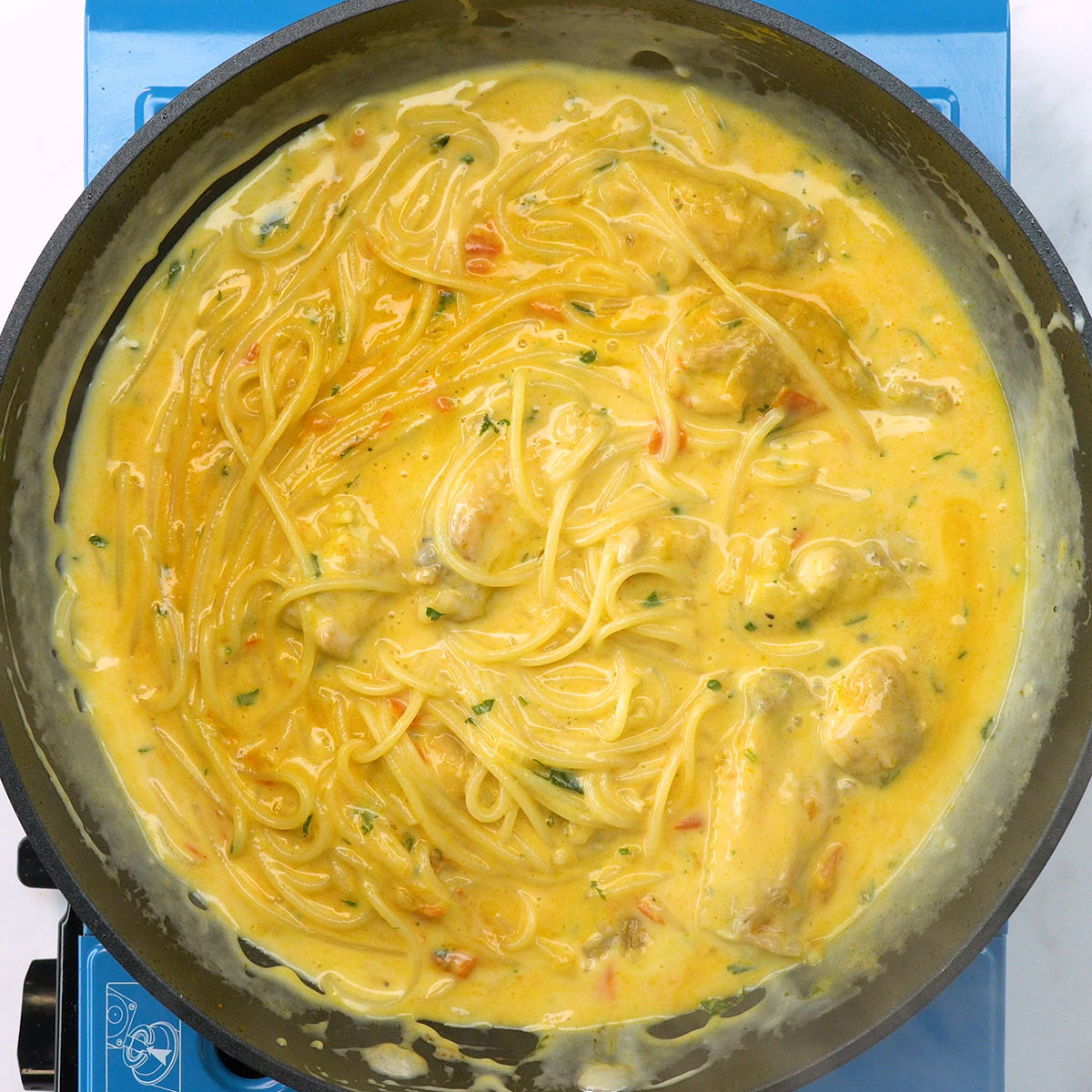 Espaguete misturado com molho branco e frango temperado.