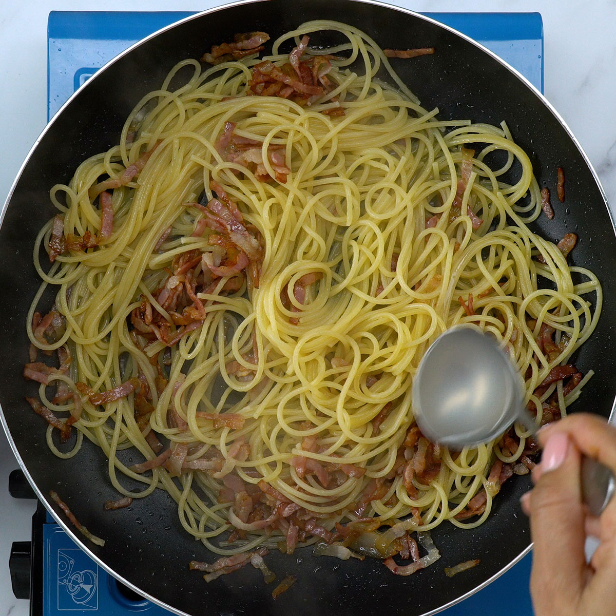 Água do cozimento sendo adicionada ao espaguete carbonara.